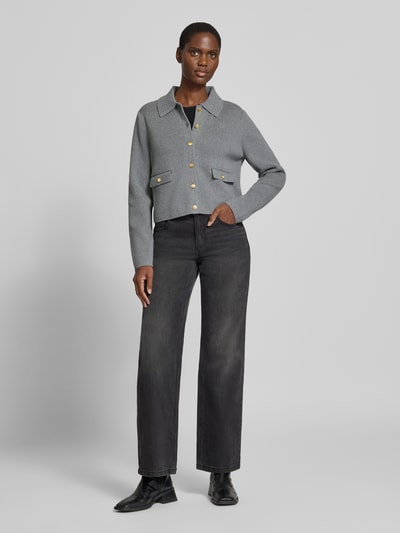 Frauenmodel trägt Strickjacke aus Baumwoll-Woll-Mix von Tommy Hilfiger in Uni-Grau mit Zierknöpfen, Brusttaschen und Kragen, Cropped-Länge, Strickoptik, Ganzkörperansicht von vorne.