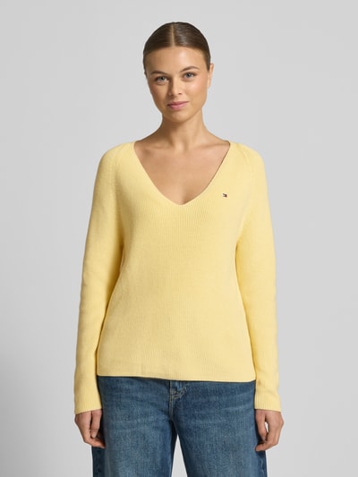 Modelka kobieca nosi Regular Fit Strickpullover aus reiner Baumwolle od Tommy Hilfiger, żółty rippstrick, V-dekolt, logo, widok z przodu, ujęcie całej sylwetki.