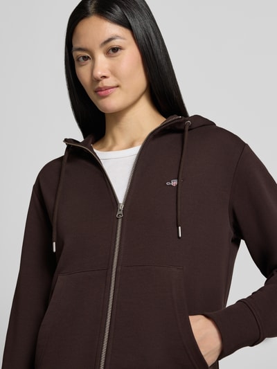 Vrouwenmodel draagt Regular fit sweatjack van katoenmix van GANT in donkerbruin met kleine logo, dames sweatjack, close-up bovenlichaam.