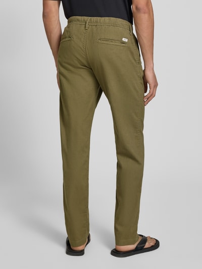 Männermodel trägt Relaxed Fit Hose aus Baumwoll-Leinen-Mix Modell 'KANE' von Jack & Jones in Oliv mit elastischem Bund und Gesäßtaschen, Ganzkörperansicht Rückansicht.