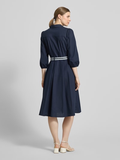 Frauenmodel trägt Hemdblusenkleid mit V-Ausschnitt und Bindegürtel von More & More in Dunkelblau, Baumwoll-Elasthan-Mix, A-Linie, Midikleid, Knopfleiste, Rückenlänge 109 cm, Brustweite 47 cm, Ärmellänge 49 cm, Ganzkörperansicht Rückansicht.