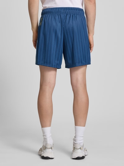 Männermodel trägt Loose Fit Trikot-Shorts mit FIGC-Applikation von adidas Originals, Optik: Allover-Muster, Materialverarbeitung: Jacquard, Kontraststreifen, seitliche Eingrifftaschen, elastischer Bundabschluss mit Tunnelzug, Ganzkörperansicht Rückansicht.