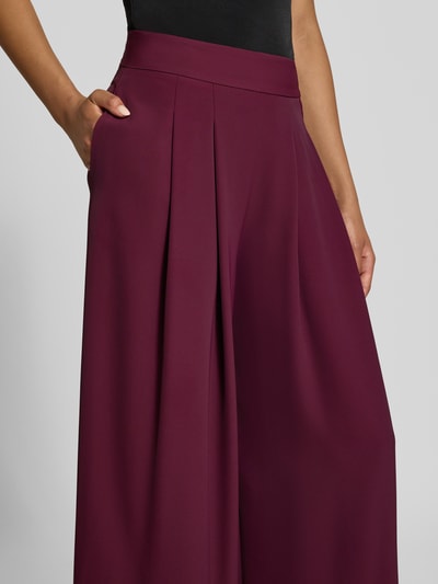 Frauenmodel trägt Wide Leg Stoffhose mit Reißverschlusstaschen von Rinascimento in dunklem Bordeaux, glatte Textur, Nahaufnahme Oberkörper. Material-Mix mit Stretch-Anteil, elastischer Bund, seitliche Reißverschlusstaschen, Bundweite bei Größe S 37 cm, Innenbeinlänge bei Größe S 82 cm.