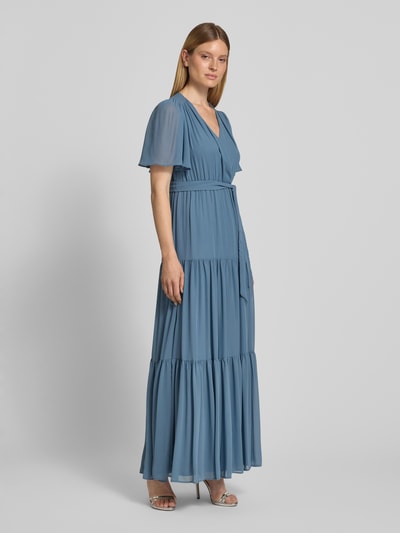 Frauenmodel trägt Abendkleid mit V-Ausschnitt und Bindegürtel von Christian Berg Cocktail aus Chiffon in Blau, A-Linie, Stufen-Look, Maxikleid, Ganzkörperansicht von vorne. Rückenlänge 151 cm, Brustweite 41 cm, Ärmellänge 30 cm bei Größe 36.