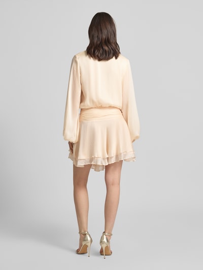 Frauenmodel trägt Minikleid mit kurzer Knopfleiste Modell 'MAGALI' von Guess in Beige, taillierter Schnitt, Volantsaum, Rückenlänge 88 cm, seitlicher Knopf- und Reißverschluss, Ganzkörperansicht Rückansicht.