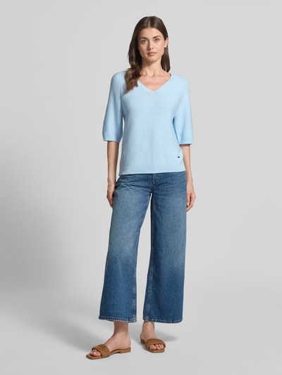 Frauenmodel trägt Regular Fit Strickpullover aus Baumwoll-Mix von s.Oliver RED LABEL, Optik: Unifarben, V-Ausschnitt, Kurzarm, Raglanärmel, gerippte Abschlüsse, Struktur: Strick, Materialverarbeitung: Baumwoll-Mix, Logo-Applikation und Label-Applikation aus Metall, Hellblau, Ganzkörperansicht von vorne.