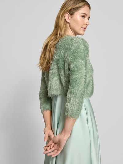 Frauenmodel trägt Bolero aus Kunstfell mit Viskose-Anteil von V.M., Material-Mix in sanftem Grün, 3/4-Arm, Rückenlänge 36 cm, Ganzkörperansicht Rückansicht.