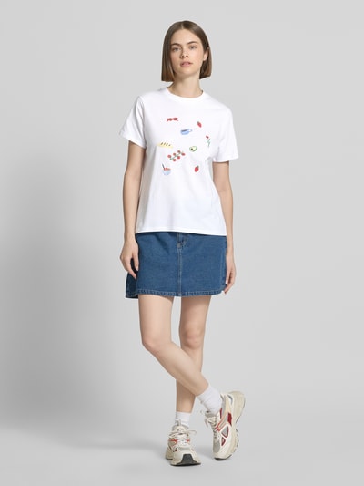 Frauenmodel trägt Damen T-Shirt von Pieces, Modell 'GAK', Optik: Unifarben, Passform: Regular-Fit, Applikation: Stickerei, Rundhals-Ausschnitt, Ärmelform: Kurzarm, Reine Baumwolle, weiße, glatte Textur auf Jeansrock, Ganzkörperansicht von vorne.
