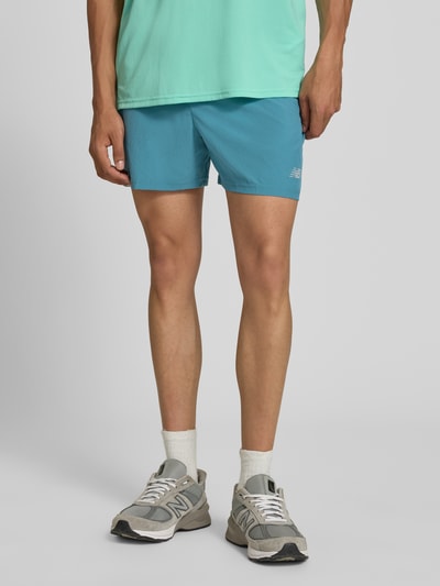Männermodel trägt Shorts mit elastischem Bund und Logo von New Balance in Blau, Regular-Fit, mit Tunnelzug und Logo, Nahaufnahme Unterkörper.