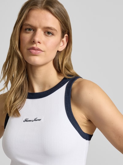 Vrouwenmodel draagt Tanktop in Ripp-Optik met Label-Stitching van Guess Jeans, wit met donkerblauwe boorden, katoenmix met modal, slim fit, riblook, labelstitching, ruglengte bij maat S 50 cm. Close-up bovenlichaam vooraanzicht.