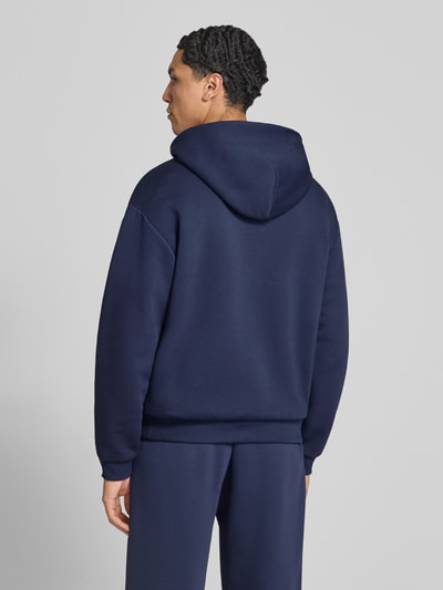 Männermodel trägt Hoodie mit Logo-Print von REVIEW aus Baumwoll-Mix in Dunkelblau, lockere Passform, Ganzkörperansicht Rückansicht.