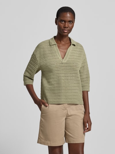 Modelka kobieca ma na sobie Strickpullover mit V-Ausschnitt und 3/4-Arm Modell 'Garakino' od OPUS, bawełna, relaxed fit, kołnierz polo, długość tyłu 56 cm, długość rękawa 33 cm, kolor jasna oliwka, faktura prążkowana, przód w całości widoczny, zdjęcie całej sylwetki z przodu.