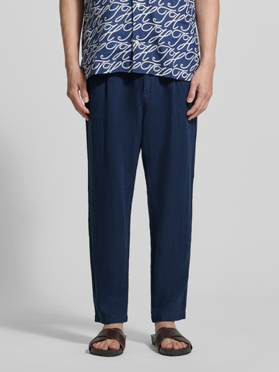 Mannenmodel draagt Tapered Fit Leinenhose mit Eingrifftaschen van MCNEAL in zuiver linnen, indigo blauw, steekzakken, tapered fit, bandwijdte maat M 45 cm, binnenbeenlengte maat M 76 cm, paspelzakken achter. Detailopname onderlichaam.