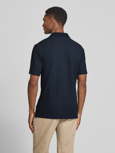Männermodel trägt Slim Fit Poloshirt mit Strukturmuster und V-Ausschnitt von bugatti aus reiner Baumwolle in Dunkelblau, Ganzkörperansicht Rückansicht.