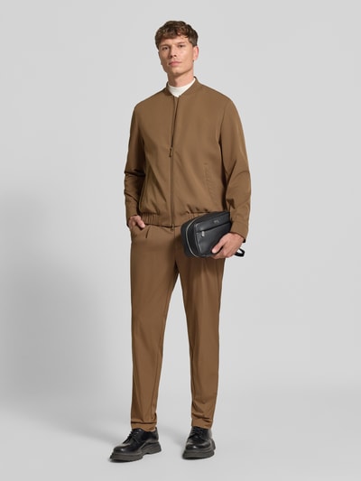 Männermodel trägt Kosmetiktasche mit Label-Detail Modell 'Ray EVO' von BOSS in Schwarz, Kunstleder mit Struktur, Ganzkörperansicht von vorne.