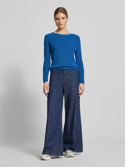Vrouwenmodel draagt Regular Fit gebreide pullover uit puur katoen van Tommy Hilfiger in blauwe tricotlook met logo-opschrift, lange mouw, ronde hals, geribde mouwboorden en rompzoom, geheel van voren gezien