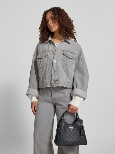 Frauenmodel trägt Handtasche mit Logo-Muster Modell 'ECO MERIDIAN II' von Guess mit Label-Applikation, Tragehenkel, Schulterriemen und Reißverschluss, Hauptfach, Maße: Breite 27 cm, Länge 21 cm, Tiefe 12 cm, Schulterriemen 120 cm, Ganzkörperansicht von vorne.