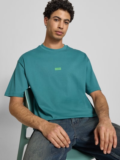 Männermodel trägt Oversized T-Shirt aus reiner Baumwolle Modell 'NALONO' von Hugo Blue in Uni-Türkis mit Label Print, Nahaufnahme Oberkörper.