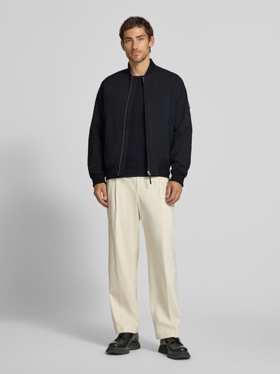 Męski model nosi bomberkę z zamkiem błyskawicznym i wpuszczanymi kieszeniami Bomberjacke mit Reißverschluss und Eingrifftaschen od JACK & JONES premium w kolorze czarnym, krój regular fit, stójka, długość tyłu w rozmiarze M: 66 cm, szerokość ramion w rozmiarze M: 42 cm, szerokość klatki piersiowej w rozmiarze M: 60 cm, długość rękawów w rozmiarze M: 68 cm, pełny widok z przodu