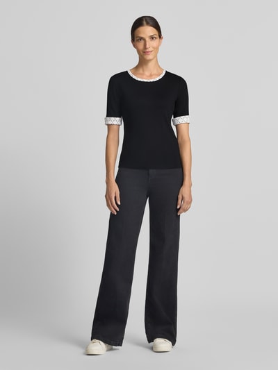 Modelka nosi Damski t-shirt 'T-Shirt in Ripp-Optik mit Rundhalsausschnitt' od Marc Cain, mieszanka bawełny i elastanu, krój slim fit, efekt prążkowania, okrągły dekolt, rękawy z zakładką, długość tyłu w rozmiarze 36: 56 cm, kolor czarny z białymi detalami, pełny widok z przodu.