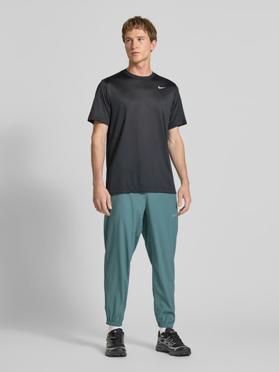 Männermodel trägt Form Pants mit Logo-Print und Eingrifftaschen von NIKE TRAINING in Türkis, körpernaher Schnitt, Ganzkörperansicht von vorne.