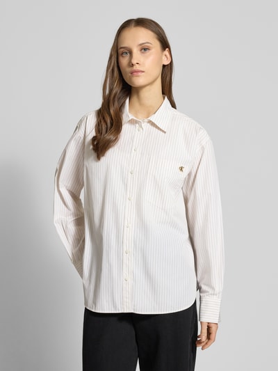 Modelka nosi Relaxed Fit Bluse mit Brusttasche und Label-Stitching von Calvin Klein Jeans, biała bawełna, krój relaxed fit, kieszeń na piersi, wyszywane logo, kołnierzyk koszulowy, długość tyłu w rozmiarze S: 69 cm, długość rękawa: 58 cm, widok całej sylwetki z przodu.