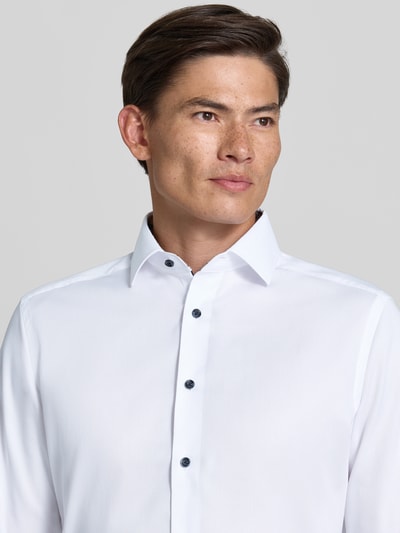 Mężczyzna nosi Modern Fit Businesshemd aus reiner Baumwolle od OLYMP, gładka biała tkanina, wyraziste ciemne guziki, zbliżenie na górną część ciała, kontekst: koszule biznesowe