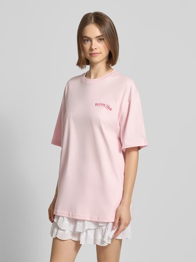 Vrouwenmodel draagt Oversized T-shirt met Statementprint van REVIEW in lichtroze, puur katoen, oversized fit, ronde hals, ruglengte bij maat S 70 cm, close-up vooraanzicht.