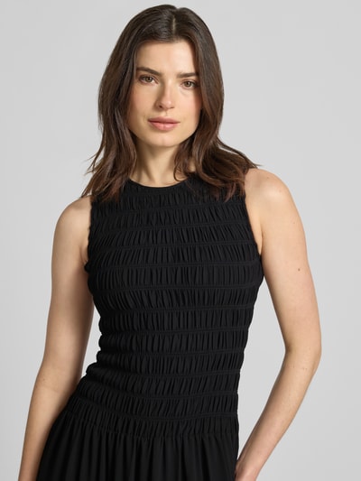 Frauenmodel trägt Maxikleid mit Smok-Details und Volantsaum von MICHAEL Michael Kors in Schwarz, Taillierter Schnitt, Rundhalsausschnitt, Nahaufnahme Oberkörper. Rückenlänge bei Größe S: 141 cm, Brustweite bei Größe S: 31 cm.