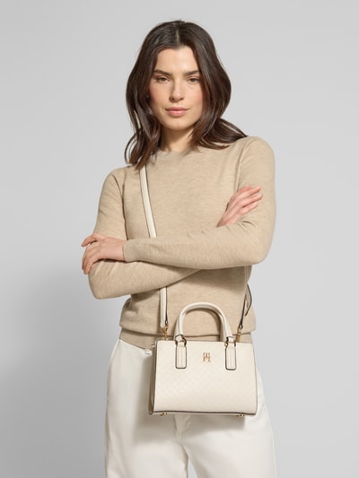 Frauenmodel trägt Henkeltasche mit Allover Logo-Prägung von Tommy Hilfiger in Beige aus Kunstleder, unifarben, Nahaufnahme Oberkörper.