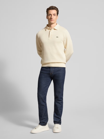 Męski model ma na sobie Regular Fit Sweatshirt aus reiner Baumwolle od Lacoste, kremowy kolor, jednolita faktura, krój regular fit, logo wyszywane, polokołnierz, długi rękaw, bawełna, dzianina prążkowana, widok całej sylwetki z przodu.