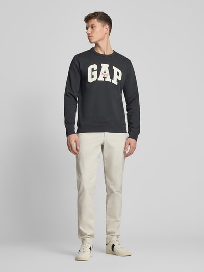 Männermodel draagt Sweatshirt mit Logo und Rundhalsausschnitt van GAP in zwart, katoenmix, regular fit, logoprint, ruglengte maat M 69 cm, mouwlengte maat M 65 cm, Ganzkörperansicht van voren.