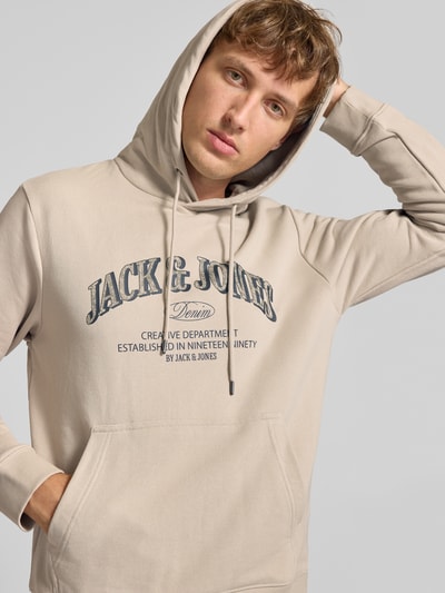 Männermodel trägt Regular Fit Hoodie aus Baumwoll-Mix Modell 'Denver' von JACK & JONES in Beige mit Kapuze, Känguru-Tasche, Nahaufnahme Oberkörper. Kontext: Herren Hoodie von JACK & JONES, Baumwoll-Mix, Regular Fit, Modell 'Denver', Kapuze mit Tunnelzug, Känguru-Tasche, elastische Abschlüsse.