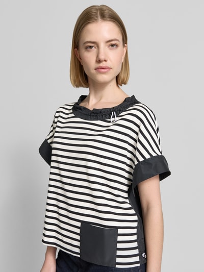 Frauenmodel trägt T-Shirt mit Rundhalsausschnitt und Kordelzug von Marc Cain, schwarz-weiß gestreift mit Eingrifftasche, gerader Schnitt, Label-Detail, Ganzkörperansicht von vorne.