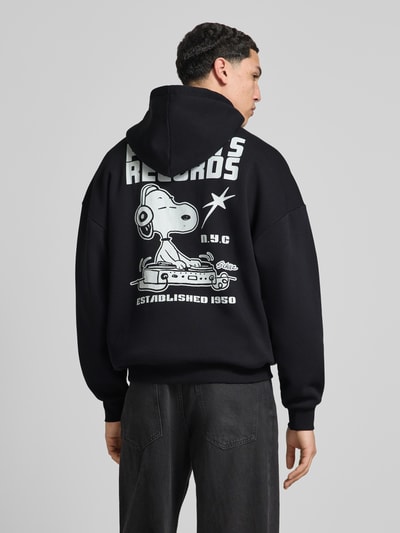 Męski model nosi Oversized Hoodie aus Baumwoll-Mix Modell 'PEANUTS BACK' von Only & Sons, czarny z nadruk peanuts®, mieszanka bawełny, kieszeń kangurka, kaptur z tunelem, długie rękawy, widok sylwetki z tyłu