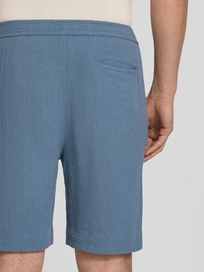 Männermodel trägt Regular Fit Shorts aus reiner Baumwolle Modell 'REGCAL' von SELECTED HOMME in Blau, Strukturstoff, Ganzkörperansicht Rückansicht.