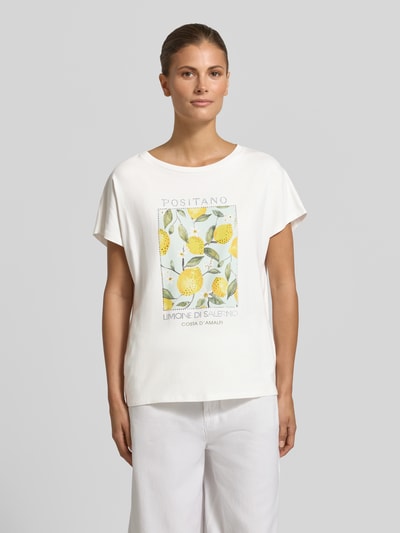 Kobiece modelka nosi t-shirt z nadrukiem z motywem i obszyciem ozdobnymi kamieniami od Oui, mieszanka bawełny i modalu, krój regular fit, okrągły dekolt, długość tyłu w rozmiarze 36: 59 cm, jasne kolory z żółtymi i zielonymi akcentami, gładka faktura, widok całej sylwetki z przodu.