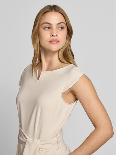 Modelka nosi Regular Fit Jumpsuit mit Bügelfalten von Betty Barclay z elastycznej mieszanki materiałów, jasny kolor, krótki rękaw, Nahaufnahme górnej części ciała. Długość tyłu w rozmiarze 36: 133 cm, szerokość w rozmiarze 36: 47 cm, całkowita długość w rozmiarze 36: 40 cm, długość wewnętrzna nogawki w rozmiarze 36: 62 cm.