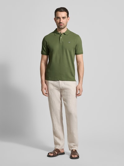 Männermodel trägt Slim Fit Poloshirt mit Logo-Stitching von Gant in Grün, Reine Baumwolle, Polo-Kragen, Kurzärmelig, Ganzkörperansicht von vorne.