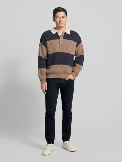 Męski model nosi Tapered Fit Jeans mit Label-Detail Modell 'Lyon' od Pierre Cardin, mieszanka bawełny z dodatkiem streczu, krój tapered fit, szerokość w pasie 39 cm, długość wewnętrzna nogawki 79 cm, ciemny jeans, gładka tekstura, widok całej sylwetki z przodu.