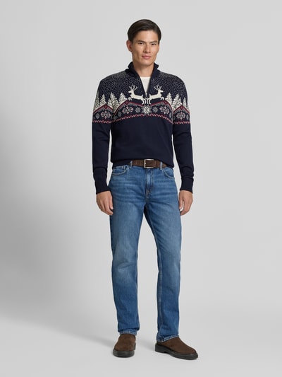 Männermodel trägt Regular Fit Strickpullover aus reiner Wolle Modell 'Dale' von Dale of Norway, Troyer-Kragen, Muster in Dunkelblau und Weiß, Herren Strickpullover, Ganzkörperansicht von vorne.