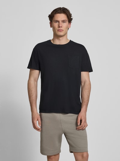 Männermodel trägt T-Shirt aus Baumwoll-Leinen-Mix mit Brusttasche von Superdry, męski t-shirt, krój regular fit, okrągły dekolt, brustasza, długość tyłu w rozmiarze M: 66 cm, czarny kolor, prosta faktura, całkowity widok z przodu.