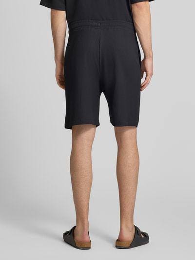 Männermodel trägt Shorts in Plissee-Optik mit elastischem Bund von REVIEW, Schwarz, Regular-Fit, Material-Mix mit Stretch-Anteil, Ganzkörperansicht Rückansicht.