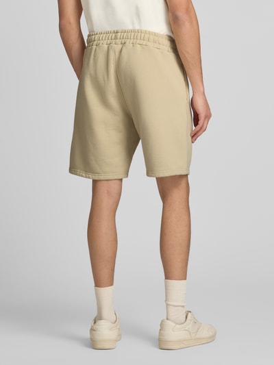 Männermodel trägt Shorts mit elastischem Bund und Logo-Stitching von Pegador aus Baumwoll-Mix in Beige, Loose-Fit, Ganzkörperansicht Rückansicht.