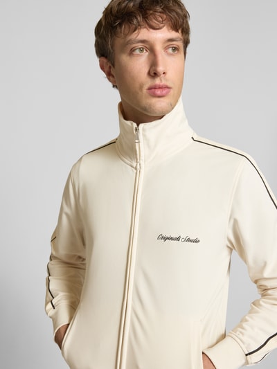 Männermodel trägt Slim Fit Sweatjacke mit Logo-Stitching Modell 'Niagara' von Jack & Jones in Creme, Stehkragen, Reißverschluss, Nahaufnahme Oberkörper.