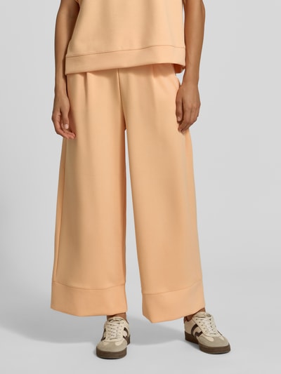 Frauenmodel trägt Wide Leg Sweatpants aus Modal-Mix von Rich & Royal in Apricot mit elastischem Bund, Bundfalten und Eingrifftaschen, Nahaufnahme Unterkörper.