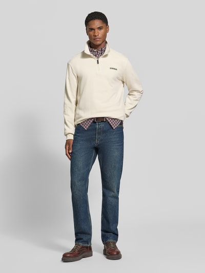 Männermodel trägt Relaxed Fit Sweatshirt aus elastischem Baumwoll-Mix von Napapijri in Creme mit Label-Detail und Troyer-Kragen, Ganzkörperansicht von vorne.