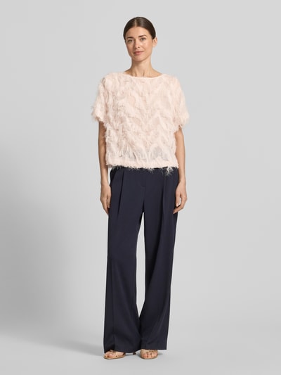 Modelka kobieca ma na sobie Boxy Fit Blusenshirt mit Fransen-Design Modell 'MYLINE' od Selected Femme, jasnoróżowy, strukturalny, z frędzlami, półprzezroczysty chiffon, krótkie rękawy, dekolt łódka, proste szerokie spodnie, widok całej sylwetki z przodu.