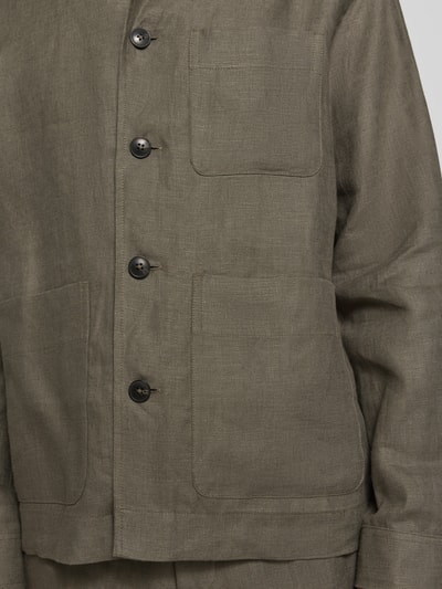 Męski model nosi koszulę wierzchnią Regular Fit Overshirt aus reinem Leinen model 'BAIRD' von SELECTED HOMME, efekt: jednolity kolor, krój regular fit, wykładany kołnierz, listwa guzikowa, długi rękaw, brustasza, nakładana boczna kieszeń, wykończenie materiału: tkanina lniana, materiał: len; detal: zbliżenie na górną część.