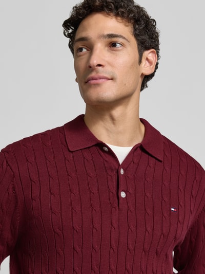 Männermodel trägt Regular Fit Pullover aus reiner Baumwolle von Tommy Hilfiger in Dunkelrot mit Strukturmuster, Nahaufnahme Oberkörper.